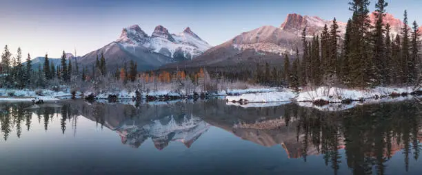 Photo of First snow Almost near perfect reflection of the Three Sisters Peaks in the Bow River. Canmore in Banff National Park Alberta Canada Snow-covered winter mountain in a winter atmosphere. Beautiful day