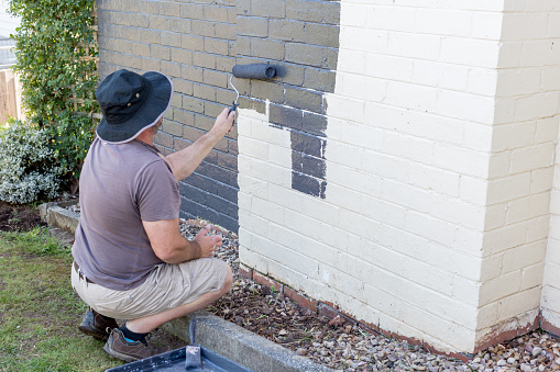 Senior man painting the exterior of a brick suburban home