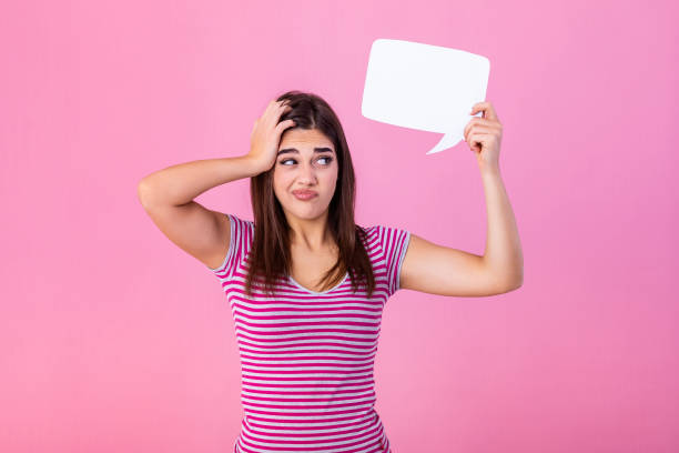 istock Beutiful young woman is holding speech bubbles, looking at camera and showing confusion, isolated on pink background 1188569855