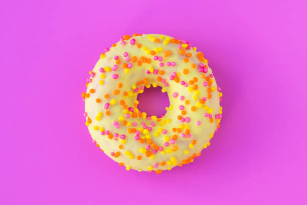 Glazed yellow donut with multicolored sprinkles on bright pink background. Unhealthy high-calorie food. Fun mood concept. Laconic food design
