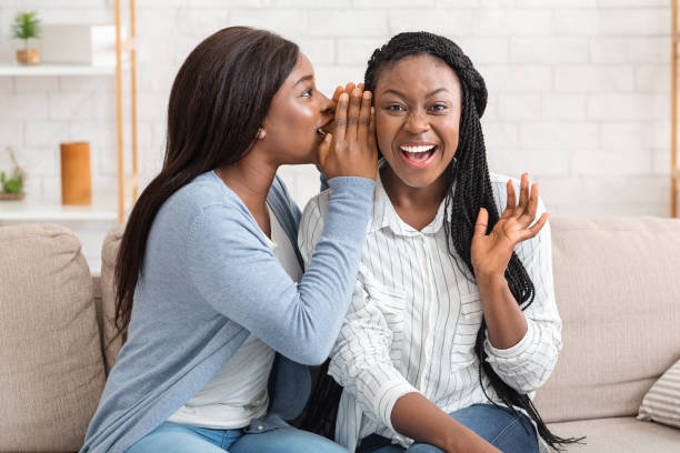 自宅でソファでうわさ話をする2人の若いアフリカ系アメリカ人女性 - whispering women talking mystery ストックフォトと画像