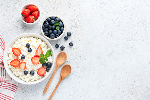 Curd cheese, cottage cheese or tvorog or ricotta with fresh berries in bowl on concrete background. Healthy dairy product, source of Calcium and Protein. Top view with copy space