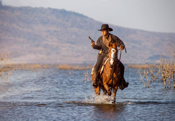 istock Man Holding Gun While Riding Horse In Lake 1188579800