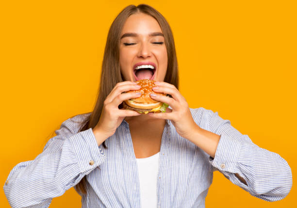 istock Hungry Woman Biting Burger Standing Over Yellow Background 1188579801