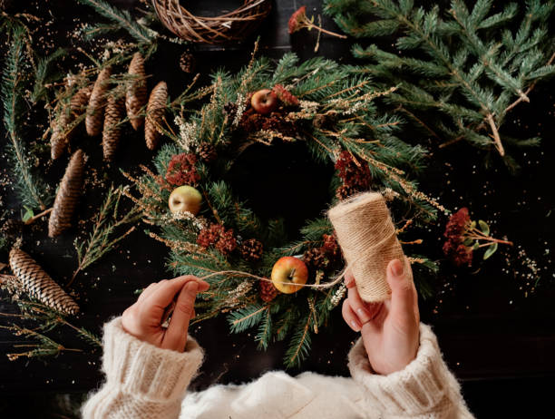 Woman in white sweater making a Christmas wreath stock photo