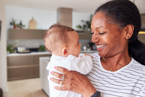 nonna amorevole che tiene in braccio una nipotina di 3 mesi in cucina a casa - baby grandparent newborn grandmother foto e immagini stock