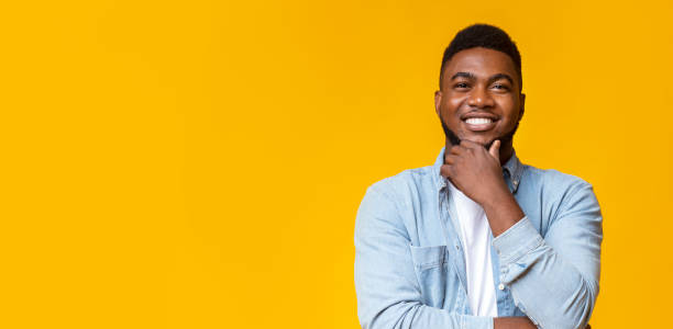 Smiling african guy touching his beard on yellow background