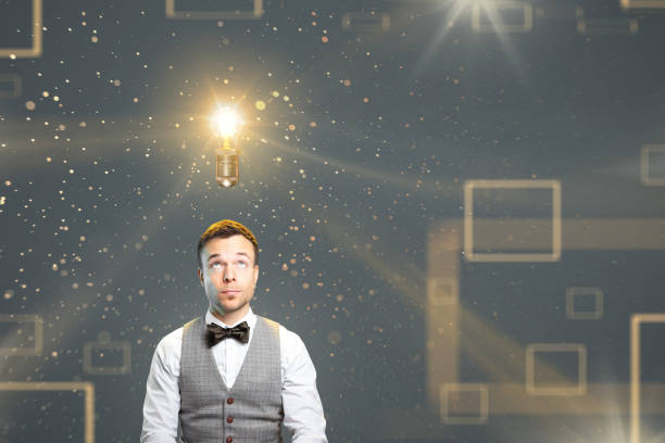 Inspired man with a light bulb above the head A man with a bow tie and waistcoat is looking towards a glowing light bulb above his head. Several light effects accompany the image. man with a light bulb over his head stock pictures, royalty-free photos & images