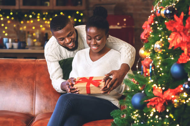 Happy black girl received Christmas present from her caring boyfriend Happy african american girl received Christmas present from her caring boyfriend, looking at gift box with excitement. beautiful women giving head stock pictures, royalty-free photos & images