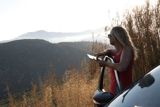 mature woman uses tablet for directions outside car at sunrise - 15828 imagens e fotografias de stock