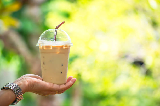 istock Glass of cold espresso coffee in hand Background blurry views tree. 1188588903