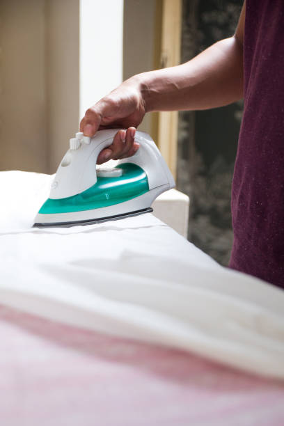 istock man using cordless iron to iron a white shirt over a pink ironing board 1188590697
