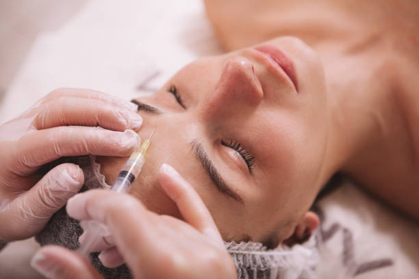 Beautiful young woman at cosmetology clinic Top view close up of a woman receiving filler injections in forehead. Professional cosmetologist injecting hyaluronic acid into skin of female client acid photos stock pictures, royalty-free photos & images