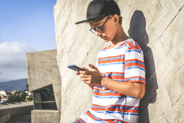 istock Boy Wearing Cap Using Smart Phone While Standing Against Wall Outdoors 1188598867