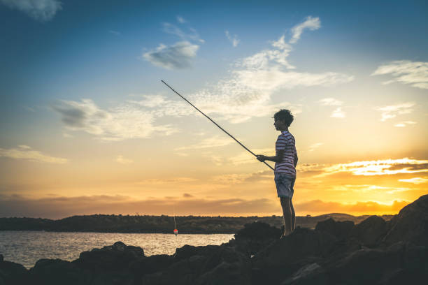 istock Side View Of Boy Fishing While Standing On Rock At Beach During Sunset 1188601488