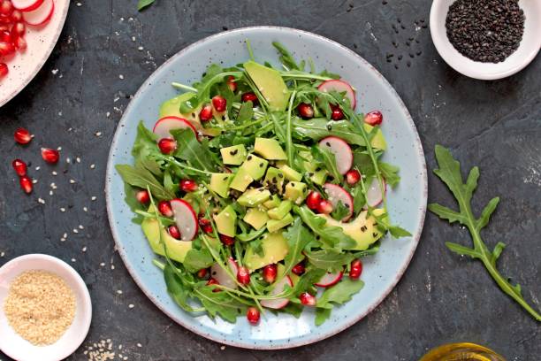 istock Ingredient for making salad on dark background. Vegetable salad in plate:avocado, arugula, pomegranate, radish and sesame. 1188603555