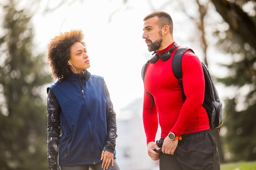 Young athletic man talking to his practice partner while standing on a jogging track in a city park.