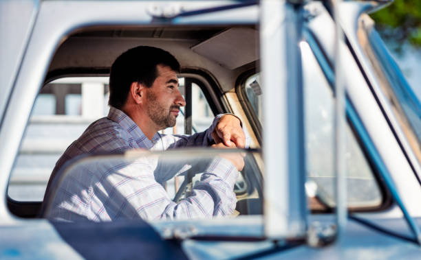 Side view of a man driving an old pick-up truck on an American ranch.