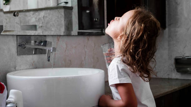 Little curly child girl rinses her mouth with water in bathroom, side view. stock photo