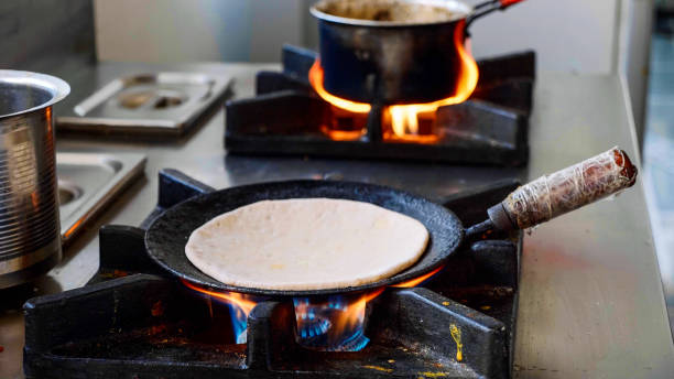 Preparing Indian aloo paratha in a frying pan on gas stove. stock photo