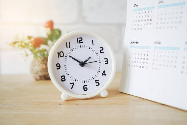 istock white analog clock , in soft focus, with blurred on wooden desk 1188608136