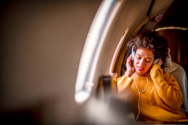 joven jovencita chic sentada en un jet privado y disfrutando de un poco de música a través de los auriculares - status symbol audio fotografías e imágenes de stock