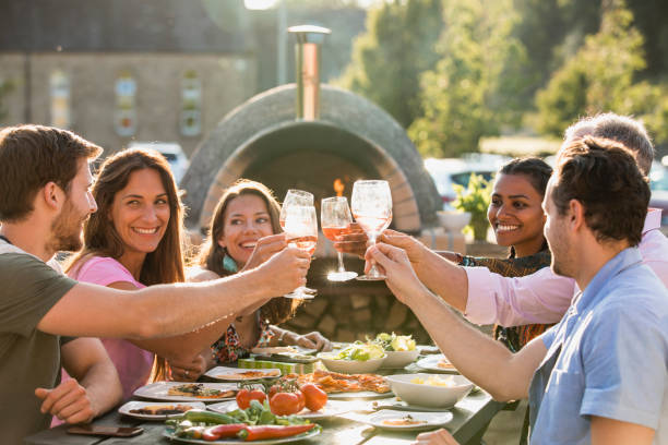 Friends Celebrating Together Friends sitting outside together eating and drinking. They are laughing together. They are toasting with their wine glasses. outdoor dining photos stock pictures, royalty-free photos & images
