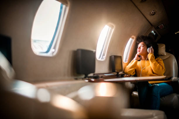 istock Young rich woman sitting on a private airplane and looking through a window while listening to music through headphones 1188608699