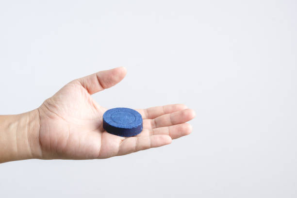 istock Hand holding automatic Bleach toilet bowl cleaner stain remover blue tab or tablet flush tank 1188609947