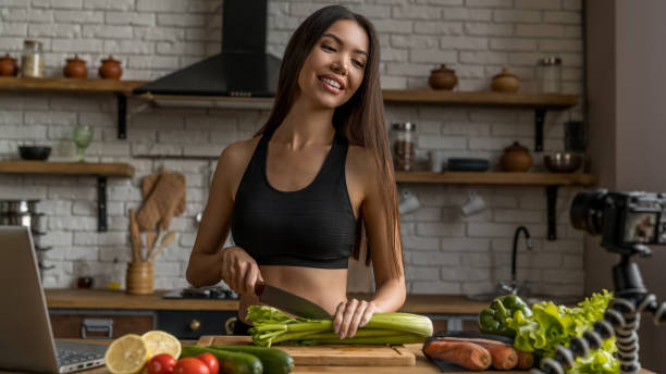 istock Smiling woman cutting celery in kitchen and recording it on video 1188611863