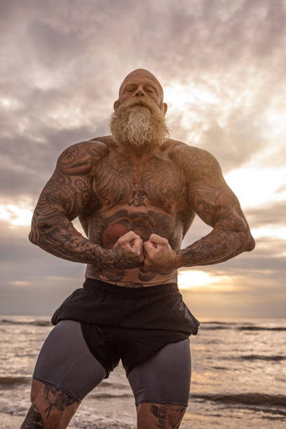 Tattooed Senior Man During beach Workout Bearded Aggressive muscular Senior Man during outdoor workout on the beach senior bodybuilders stock pictures, royalty-free photos & images