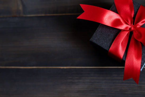 gift box white new year or Christmas Packed present container with red ribbon on Vintage Matte black wooden board background for holiday concept with copy space, top view.