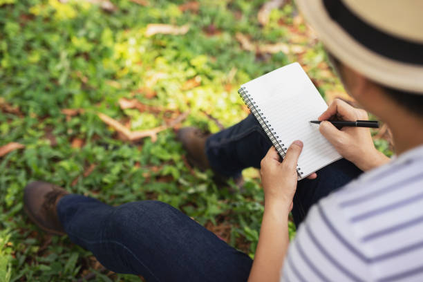 istock close up hand young man are sitting using pen writing Record Lecture notepad into the book in the park. 1188613682