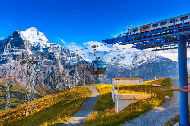 Grindelwald first cable car cabins, Switzerland Grindelwald, Switzerland cable car cabins arriving to high station First and autumn Swiss Alps mountains panorama landscape, wooden chalets on green fields, Bernese Oberland, Europe engelberg photos stock pictures, royalty-free photos & images