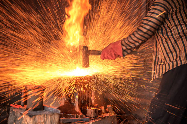 A mid adult Caucasian male blacksmith wearing gloves works intensely to shape glowing metal on an anvil in a rustic, smoke-filled workshop, surrounded by tools and machinery, in dynamic warm lighting.