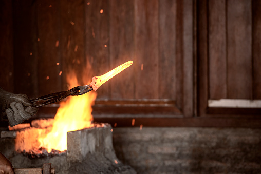 Blacksmith forging the molten metal with a hammer to make keris in the blacksmith's workshop