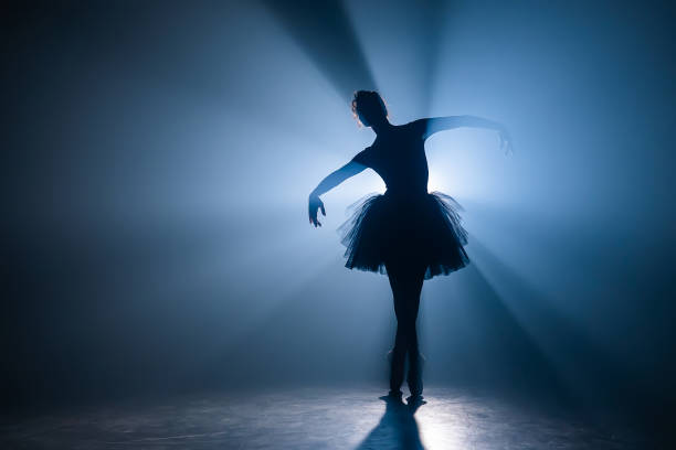 bailarina no vestido preto do tutu que dança no estágio com luz azul mágica e fumo. silhueta do dançarino atrativo novo no pointe das sapatas do bailado que executa na anoitecer. espaço de cópia. - ballet - fotografias e filmes do acervo