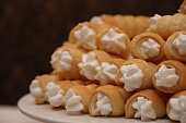 Puff pastry rolls or Schillerlocken Schaumrollen filled with cream stacked arranged on white plate copy space on dark background