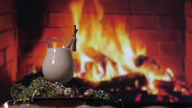 beautiful traditional eggnog cocktail prepared at home for winter parties and gatherings with friends on background of a fire by the fireplace