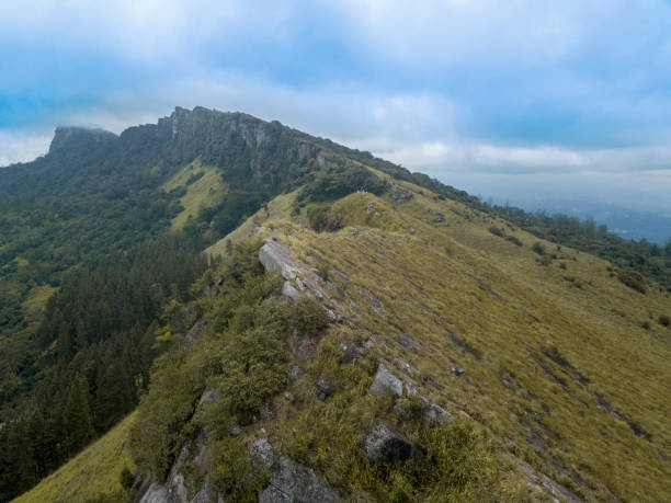 Drone landscape view of Katusu Konda edge and Uragala peak at Hanthana Mountain Range, Kandy, Sri Lanka. Surrounded by dry grass plain slopes and trees on a rocky terrain stock photo