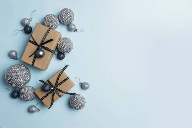 A flat lay photograph of Christmas gifts and decorations celebration the holiday season in black, silver on a blue background.