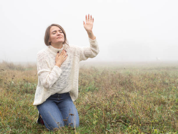 girl closed her eyes on the knees, praying in a field during beautiful fog. hands folded in prayer concept for faith - women human hand portrait eyes closed imagens e fotografias de stock