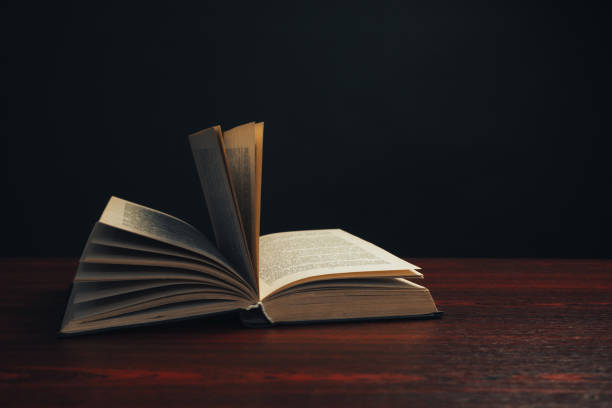istock One open old book on a red wooden table. Beautiful dark background. 1188637556