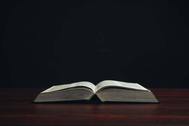 istock Open bible on a  red wooden table. Beautiful black background. 1188637571