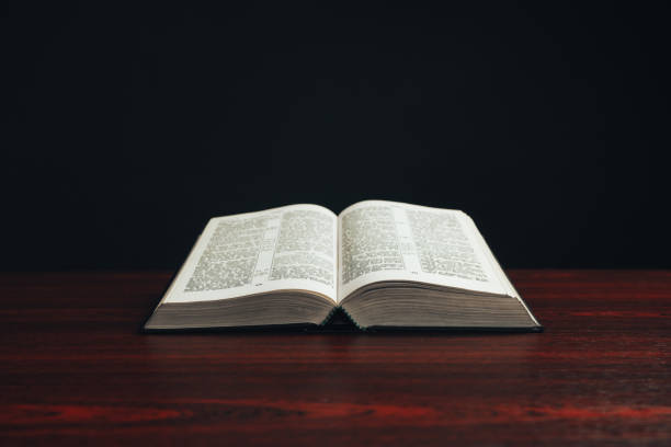 istock Open bible on a  red wooden table. Beautiful black background. 1188637667