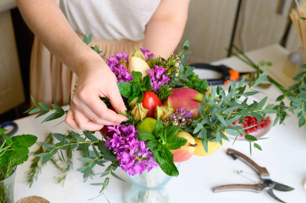 the process of forming a fruit and flower bouquet. tutorial, do it yourself. photo 27, women's hands inserts a sprig of rosemary into the bouquet