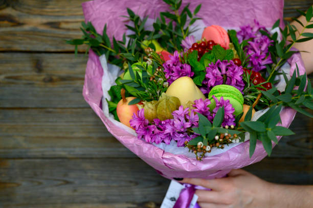 istock the process of forming a fruit and flower bouquet. tutorial, do it yourself. photo 39, women's hands holding a finished bouquet on a wooden background, space for text 1188637929
