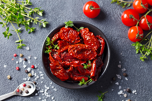 Sun dried tomatoes with fresh herbs and spices. Slate background. Top view
