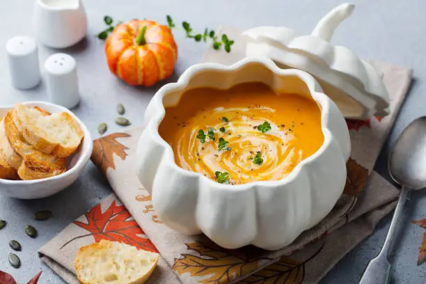 Photo of Pumpkin and carrot cream soup in creative bowl. Grey background. Close up.