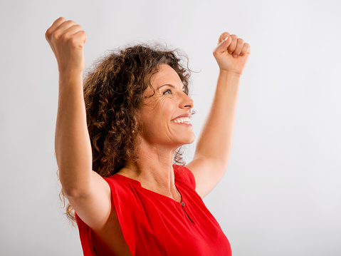 Portrait of a happy middle aged brunette with arms up expressing victory